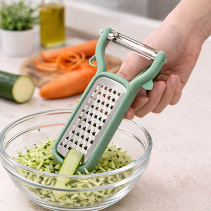 Person using a green vegetable peeler to shred a cucumber into a glass bowl on a kitchen counter.