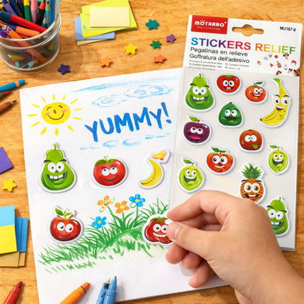 Sheet of stickers with cartoon fruits and vegetables on a wooden table with coloring supplies.