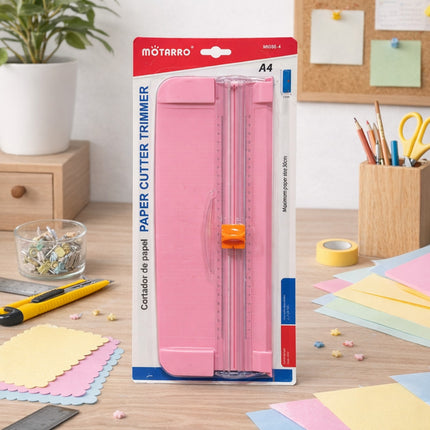 Pink paper cutter trimmer in packaging on a desk with stationery items.