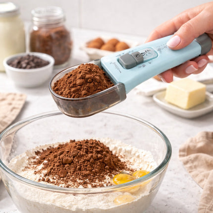 Person measuring cocoa powder into a bowl with baking ingredients on a kitchen counter.