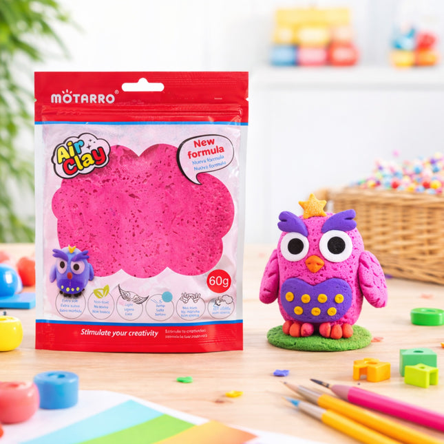 Pink owl sculpture made from Air Clay with packaging and tools on a wooden surface.