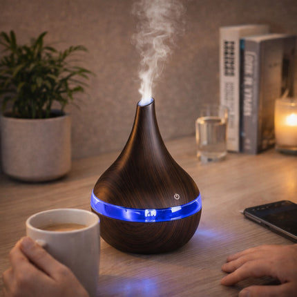 Wooden diffuser with blue light on a table next to a cup of coffee, phone, and books.
