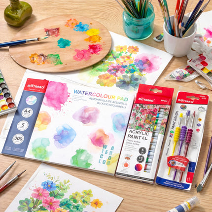 Art supplies including a watercolor pad, acrylic paint set, and brushes on a wooden table.
