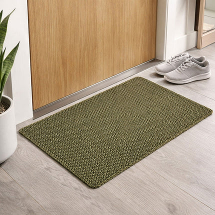 Green doormat on a wooden floor with a wooden door and white shoes in the background.
