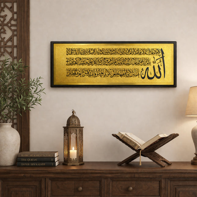 Decorative setup with framed Arabic calligraphy, lantern, and open book on a wooden surface.