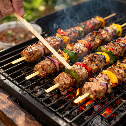 Skewers of meat and vegetables being grilled on a barbecue with a hand holding one skewer.