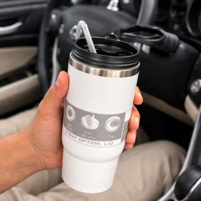 White insulated tumbler with black lid held by a hand in a car.