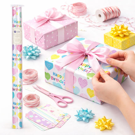 Gift-wrapping setup with colorful birthday-themed paper, scissors, and decorative bows on a white surface.