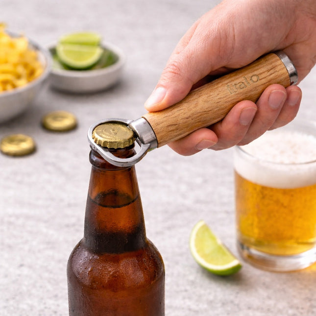 Hand using a bottle opener on a beer bottle with snacks and a glass of beer in the background.