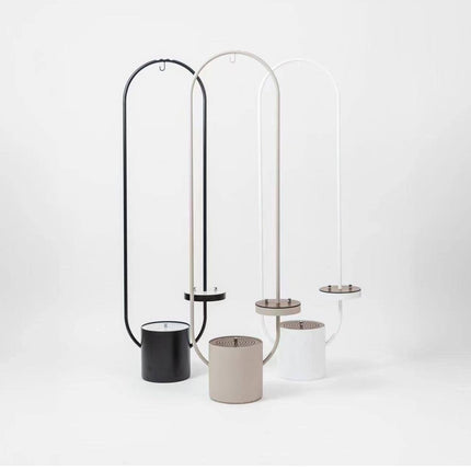 Three modern minimalist floor lamps with tall arched metal frames in black, beige, and white, each paired with a cylindrical base in matching colors, displayed on a clean white studio background.