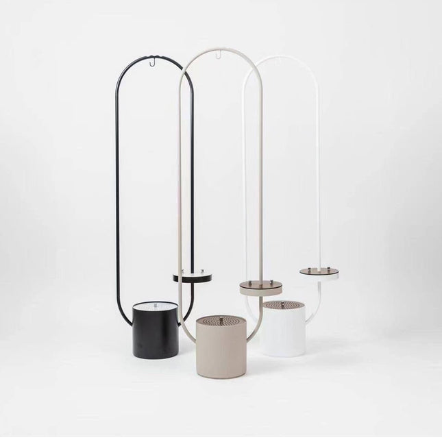 Three modern minimalist floor lamps with tall arched metal frames in black, beige, and white, each paired with a cylindrical base in matching colors, displayed on a clean white studio background.