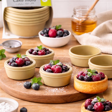Small dessert cups filled with berries on a wooden board, with a jar of honey and a cake mold in the background.