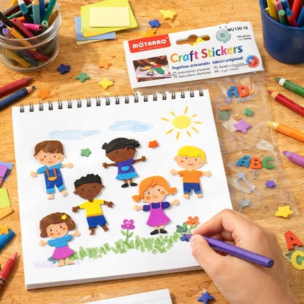 Children's craft stickers on a notebook with colorful markers and supplies on a wooden table.