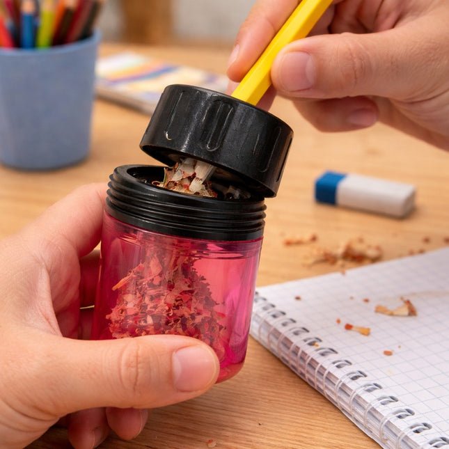 Person using a red pencil sharpener with a black top on a wooden desk.