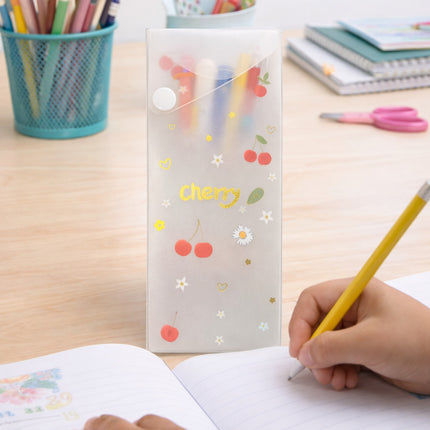 Child writing with a yellow pencil next to a transparent pouch with cherry designs on a desk.