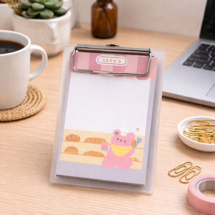 Note pad with cartoon design on a desk with coffee, laptop, and stationery items.