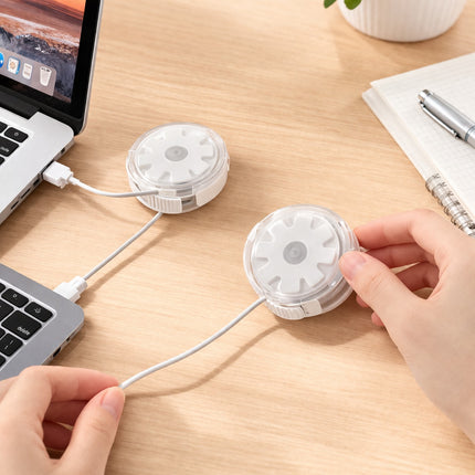 Two white cylindrical devices with USB cables on a wooden desk next to a laptop.