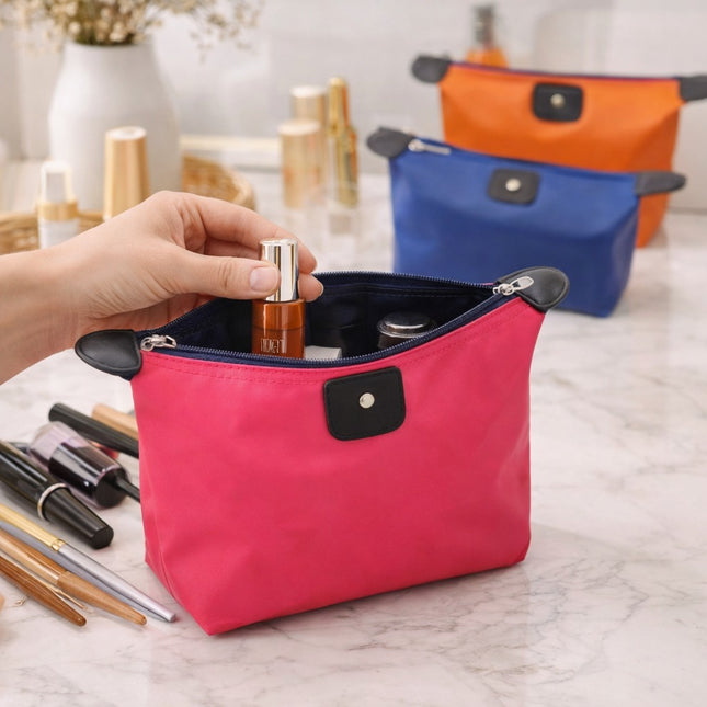 Pink makeup bag with cosmetic items on a marble surface
