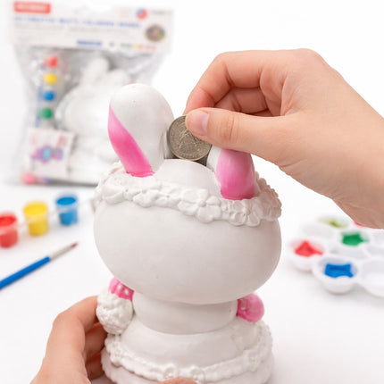 Person inserting a coin into a white rabbit-shaped piggy bank with pink ears.