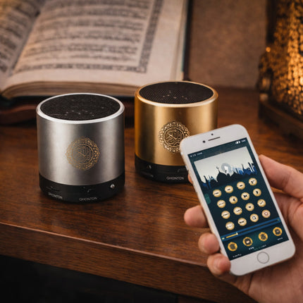 Two cylindrical speakers on a wooden surface with a smartphone displaying a music app.