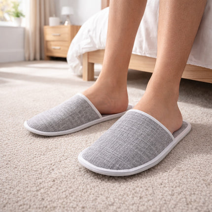 Person wearing gray slippers on a carpeted floor in a bedroom.
