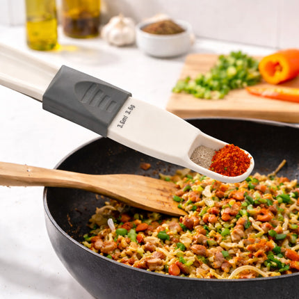 Spatula with measuring spoon adding spices to a pan of stir-fry
