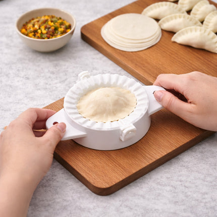 Person using a white dough press to shape dumplings on a wooden board.
