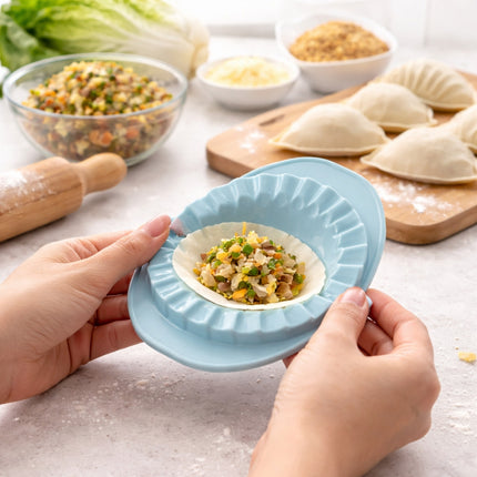 Person using a blue dough press to shape dumplings with ingredients in the background.
