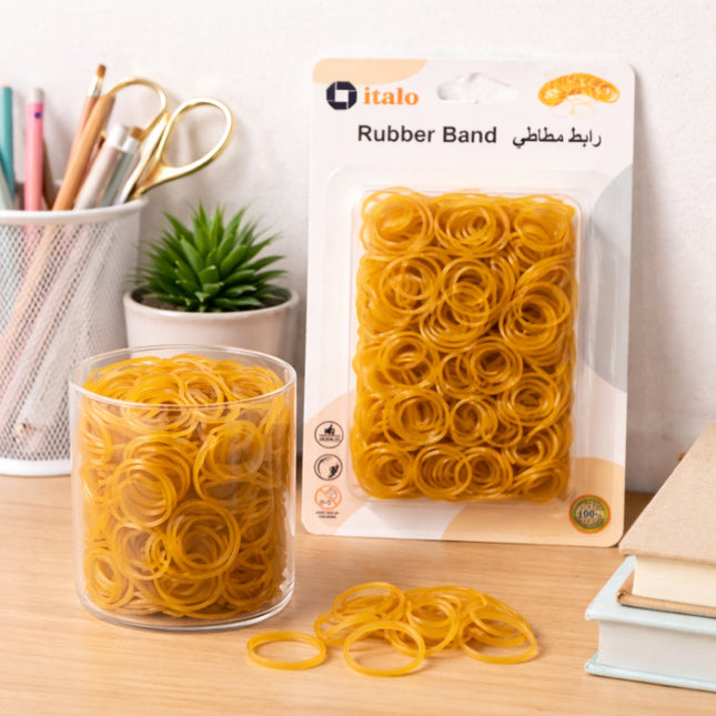 Yellow rubber bands in a clear container and packaging on a desk with stationery items.