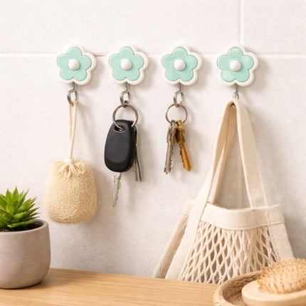 Flower-shaped hooks on a wall with keys and a bag hanging from them, next to a potted plant.