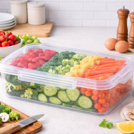 Clear container with compartments filled with fresh vegetables and fruits on a kitchen counter.