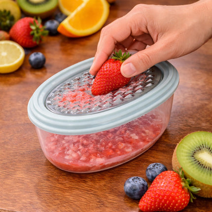 Hand using a fruit grinder with strawberries on a wooden surface surrounded by fruits.