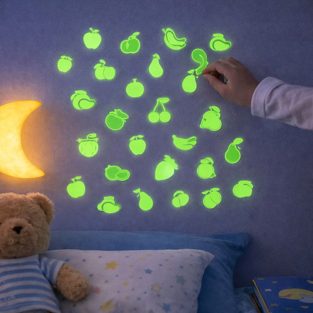 Glowing green fruit stickers on a wall with a child's hand reaching for one, next to a teddy bear and moon lamp.