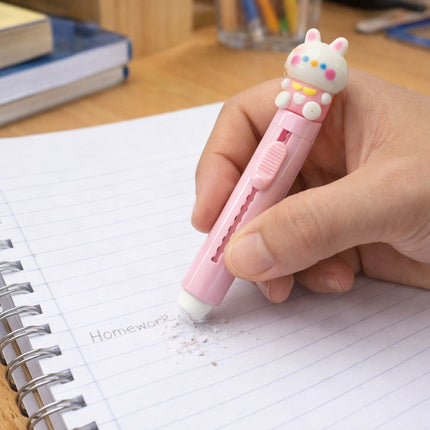 Hand holding a pink cartoon-themed pen over a notebook on a desk.