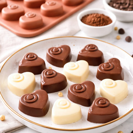 Heart-shaped chocolate candies on a white plate with a silicone mold and cocoa powder in the background.