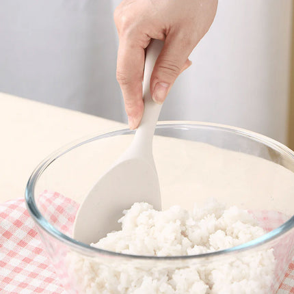 Person using a white spoon to mix rice in a glass bowl on a checkered cloth.