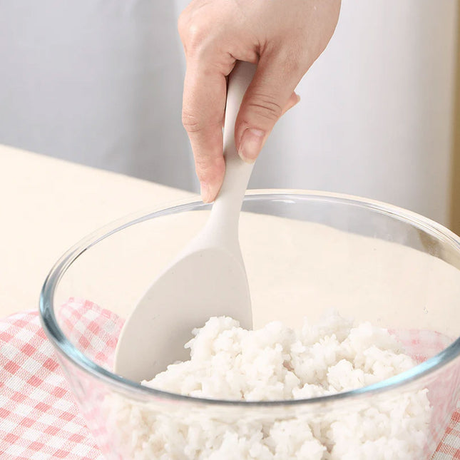 Person using a white spoon to mix rice in a glass bowl on a checkered cloth.