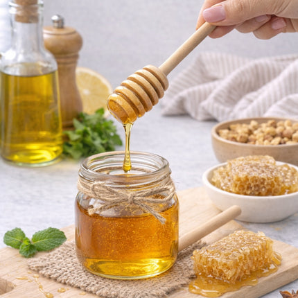 Honey being drizzled from a wooden dipper into a jar on a table with honeycomb and ingredients.