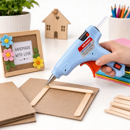 Hot glue gun being used on a craft project with cardboard and popsicle sticks.