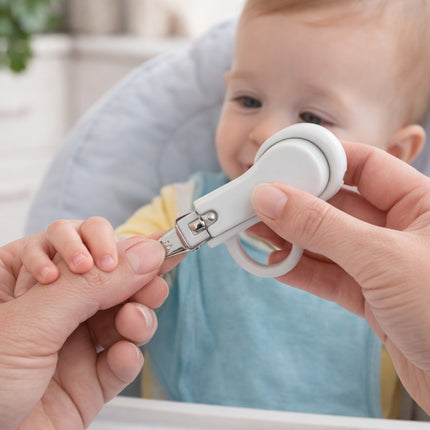 Person using a nail clipper on a baby's hand with a blurred background