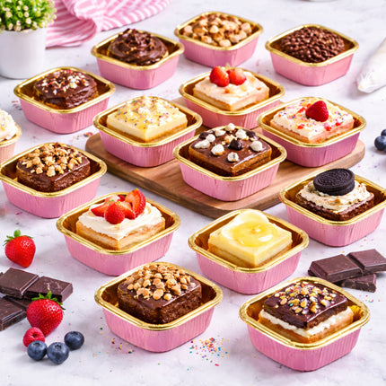 Assorted small desserts in pink containers on a white surface with berries and chocolate.