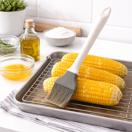 Corn on a baking tray with a brush, oil, and salt in a kitchen setting