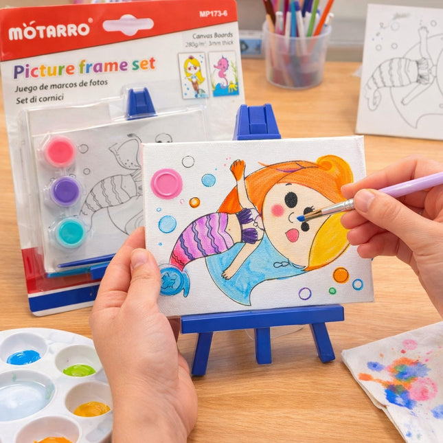 Person painting a cartoon mermaid on a small easel with art supplies around.