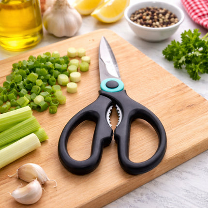 Black kitchen shears on a wooden cutting board with chopped vegetables and seasonings.