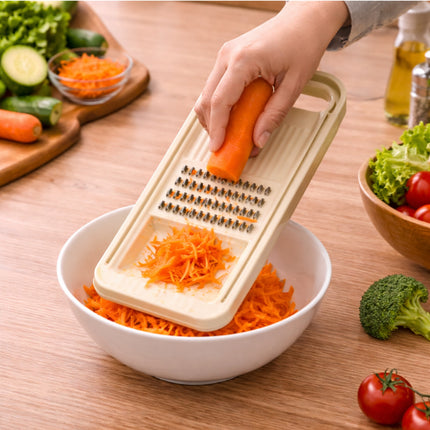 Person using a hand grater to shred carrots into a bowl on a wooden table with vegetables around.