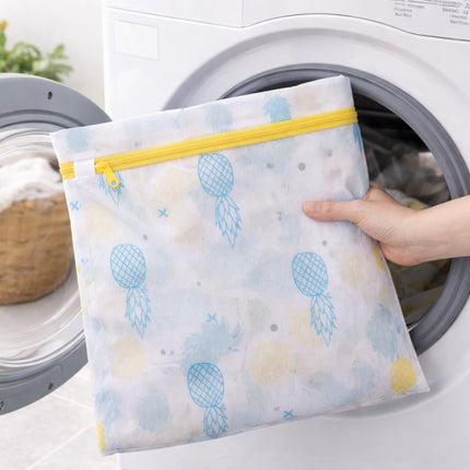 Person holding a patterned mesh laundry bag with a yellow zipper in front of a washing machine.
