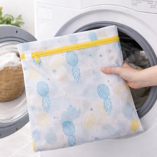 Person holding a patterned mesh laundry bag with a yellow zipper in front of a washing machine.