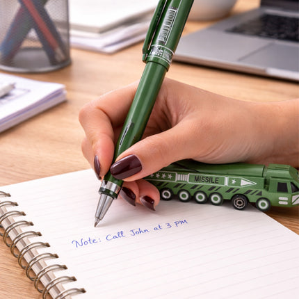Hand holding a green pen over a notebook with a toy missile launcher on a desk.