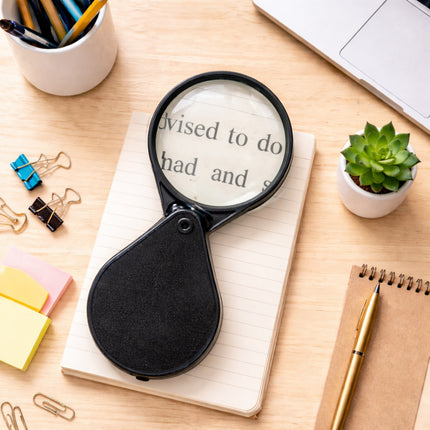 Magnifying glass on a notebook with office supplies on a wooden desk
