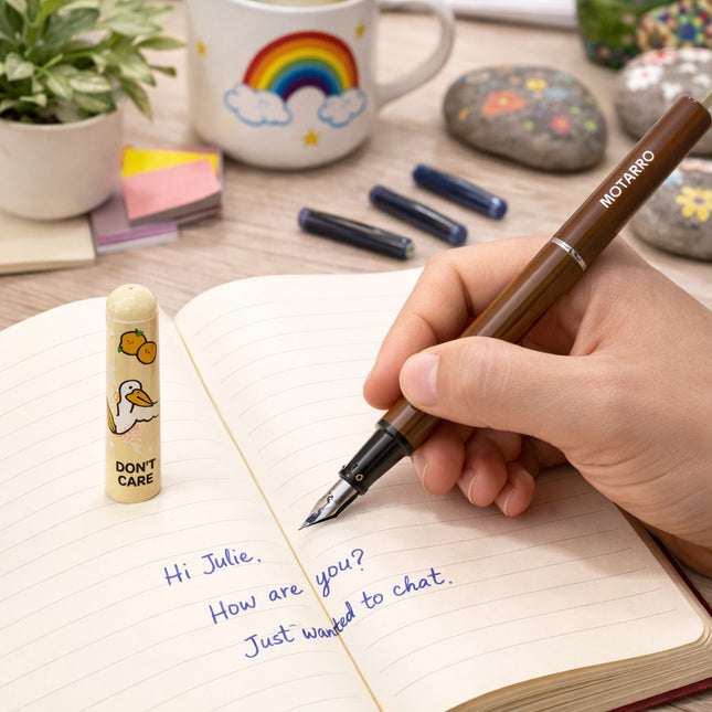 Hand writing in a notebook with a fountain pen, surrounded by stationery items on a desk.